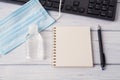 Disposable medical face mask hand sanitizer in a small bottle near spring notepad and pen on a white wood desk. Protection