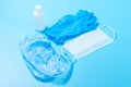 A disposable medical mask,one white bottle of antiseptic, a blue latex glove and Shoe covers on a blue background. The concept of