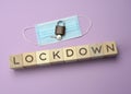 Disposable medical mask and and wooden blocks with the inscription lockdown on a purple background