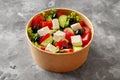 Paper bowl of colorful horiatiki salad with fresh vegetables, black olives and feta on gray stone surface Royalty Free Stock Photo