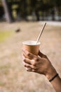 Disposable paper cup with a drinking straw in the hand of a teenager in the park on a warm day