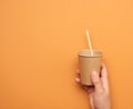 Disposable paper cup made of cardboard in a female hand, orange background