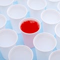 Disposable plastic white empty cups on and one glass filled with red lemonade Royalty Free Stock Photo