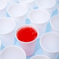 Disposable plastic white empty cups on and one glass filled with red lemonade Royalty Free Stock Photo