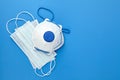 Disposable surgical face masks and white respirator on blue background, top view