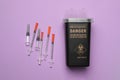Disposable syringes and sharps container on violet background, flat lay