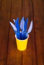 Disposable tableware, blue plastic forks standing in a yellow cup on background of wooden table Royalty Free Stock Photo