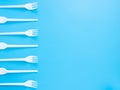 Disposable tableware, white plastic forks isolated on a blue background with copy space. Modern problems of plastic product