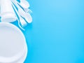 Disposable tableware, white plastic spoons, forks, glasses and plates isolated on a blue background, copy space, flat lay. Royalty Free Stock Photo