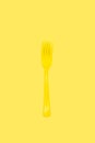 Disposable yellow plastic fork on a yellow background