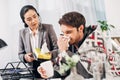 Disquieted call center operator giving napkins to sick coworker with blanket and cup