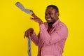 Dissatisfied african american man closes nose, feels about socks bad smell, wears casual red t -shirt in studio yellow