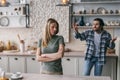 Dissatisfied angry caucasian millennial man with stubble spreads his arms to sides swears at sad blonde woman