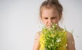 Dissatisfied capricious little girl screwing up her face looking on a bouquet of field flowers in her hands. Close up