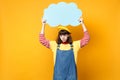 Dissatisfied girl teenager in french beret, denim sundress hold blue empty blank Say cloud, speech bubble isolated on Royalty Free Stock Photo