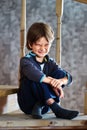 Dissatisfied grimace of little boy, 7 years old, sitting on step of wooden staircase leading to second floor of house in Royalty Free Stock Photo