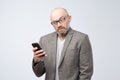 Dissatisfied man in casual suit wearing glasses reading articles, doing searching for information using phone. Royalty Free Stock Photo