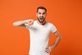 Dissatisfied irritated young man in casual white t-shirt posing isolated on orange wall background studio portrait Royalty Free Stock Photo