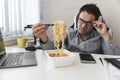 dissatisfied man eating instant noodles while working with laptop in office. Lunch at the office. tasteless junk food Royalty Free Stock Photo