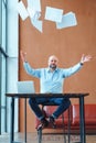 Dissatisfied mature businessman at office desk throwing paper documents in air Royalty Free Stock Photo