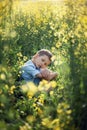 Dissatisfied preschooler boy sitting in the tall grass, propping face with hands and looking at camera