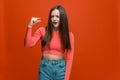 Dissatisfied pretty young girl showing small size gesture, asking little bit more on orange studio background Royalty Free Stock Photo