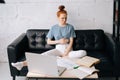 Dissatisfied redhead young businesswoman sitting at the desk with laptop computer and paper documents