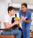 Dissatisfied surprised young man discussing documents with a doctor in the lobby of medical clinic Royalty Free Stock Photo