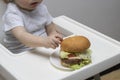 Dissatisfied toddler kid looking at a big burger picks a finger Royalty Free Stock Photo