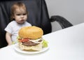 Dissatisfied toddler kid looking at a big burger. selective focus Royalty Free Stock Photo