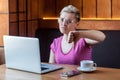 Dissatisfied young adult woman with short hair, in pink t-shirt and eyeglasses is sitting in cafe and working on laptop with Royalty Free Stock Photo