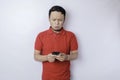 A dissatisfied young Asian man looks disgruntled wearing red t-shirt irritated face expressions holding his phone Royalty Free Stock Photo