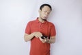 A dissatisfied young Asian man looks disgruntled wearing red t-shirt irritated face expressions holding his phone Royalty Free Stock Photo