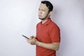 A dissatisfied young Asian man looks disgruntled wearing red t-shirt irritated face expressions holding his phone Royalty Free Stock Photo