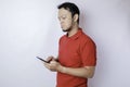 A dissatisfied young Asian man looks disgruntled wearing red t-shirt irritated face expressions holding his phone Royalty Free Stock Photo