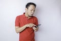 A dissatisfied young Asian man looks disgruntled wearing red t-shirt irritated face expressions holding his phone Royalty Free Stock Photo