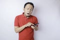 A dissatisfied young Asian man looks disgruntled wearing red t-shirt irritated face expressions holding his phone Royalty Free Stock Photo