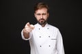 Dissatisfied young bearded male chef cook or baker man in white uniform shirt posing isolated on black background in