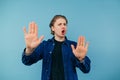 Dissatisfied young man in a shirt stands on a blue background, looks at the camera with an emotional face and shows his palms Royalty Free Stock Photo