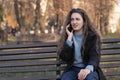 Dissatisfied young woman sits in park on bench and talks on phone and gesticulating. Girl in autumn park Royalty Free Stock Photo