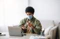 Distance education during coronavirus. Black teen student in medical mask applying antiseptic near laptop at home