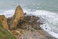 In the distance, a fisherman stands on the rocks near the war memorial of Pointe du Hoc on the Normandy coast near the town of Sai