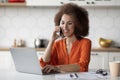 Distance Job. Young Black Female Freelancer Using Cellphone And Laptop In Kitchen Royalty Free Stock Photo