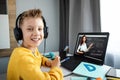 Distance learning, a boy in headphones sits at a table at home looking in a beech laptop. The concept of online education, home