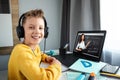 Distance learning, a boy in headphones sits at a table at home looking in a beech laptop. The concept of online education, home