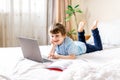 Distance learning online education. Caucasian happy boy with book studying at home with laptop notebook and doing school homework Royalty Free Stock Photo