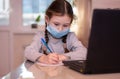 Distance learning online education.School girl in medical mask does homework on laptop at home.Quarantine Royalty Free Stock Photo