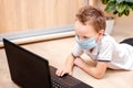 Distance learning online education. A schoolboy in a protective mask lies on the floor studying at home with a laptop and doing Royalty Free Stock Photo