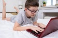 Distance learning online education, schoolboy studying at home while lying in bed with a laptop and doing school homework. Royalty Free Stock Photo