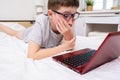 Distance learning online education, schoolboy studying at home while lying in bed with a laptop and doing school homework. e- Royalty Free Stock Photo